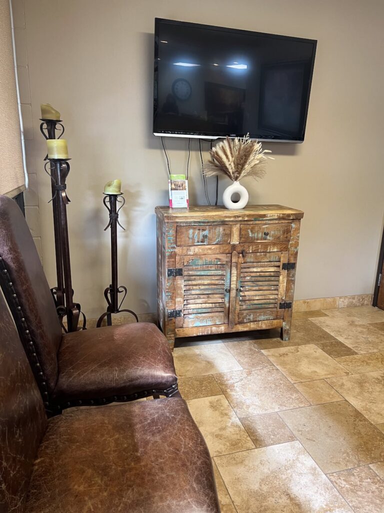 Seating area: two brown leather chairs, wooden cabinet with TV above, floor lamp, and framed artwork
