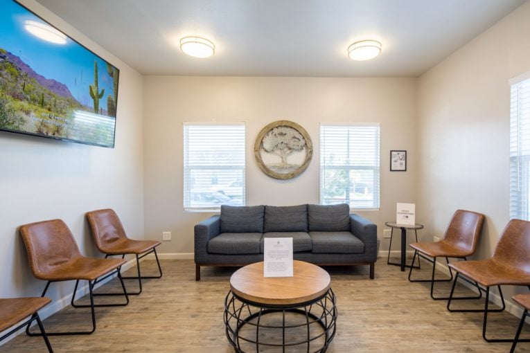 Waiting area: gray sofa, four brown leather chairs, round coffee table, wall art, and circular decorative piece