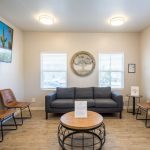 Waiting area: gray sofa, four brown leather chairs, round coffee table, wall art, and circular decorative piece