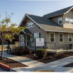 Single-story dental office with gray siding, gabled roof, front porch, and landscaped walkway under sunny sky