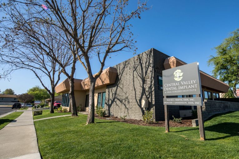 Office exterior: tan building, covered entrance, signpost with practice name and address 1116