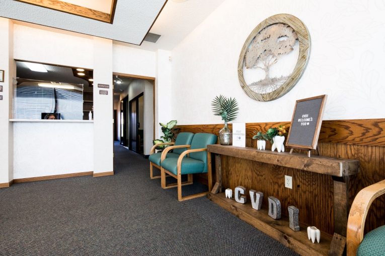 Reception area: wooden desk, circular tree artwork, teal chairs, hallway visible