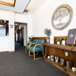 Reception area: wooden desk, circular tree artwork, teal chairs, hallway visible