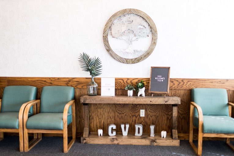 Waiting room: “CVDI” letters on wooden console, two teal chairs, plant, framed plaque.