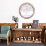 Waiting room: “CVDI” letters on wooden console, two teal chairs, plant, framed plaque.