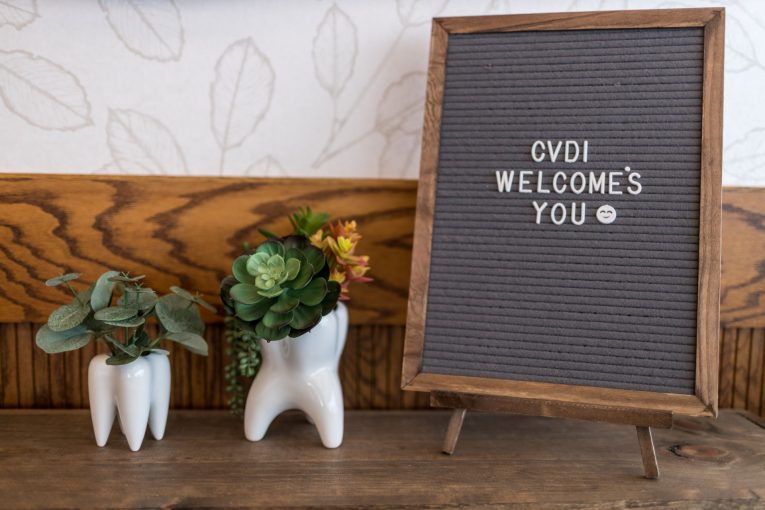 Decorative shelf: two ceramic tooth planters, green succulents, “CVDI WELCOMES YOU” letterboard