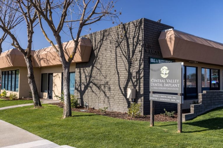 Office exterior: tan building, covered entrance, signpost with practice name and address 1116