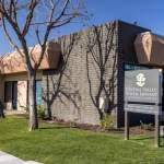 Office exterior: tan building, covered entrance, signpost with practice name and address 1116