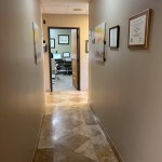 Hallway with beige walls, framed certificates, diamond-pattern tile floor, and open doorway to operatory