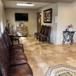 Waiting room with row of brown leather chairs, tiled floor, patterned rug, and wall-mounted TV at far end