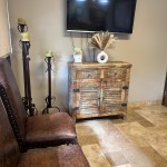 Seating area: two brown leather chairs, wooden cabinet with TV above, floor lamp, and framed artwork