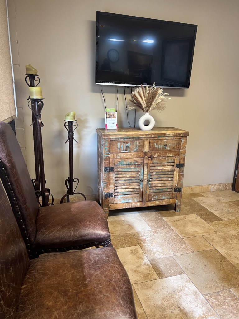 Seating area: two brown leather chairs, wooden cabinet with TV above, floor lamp, and framed artwork
