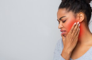 young woman having jaw pain, touching her inflamed jaw